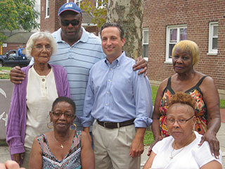 group of 6 people sitting and standing outside apartments smiling at camera