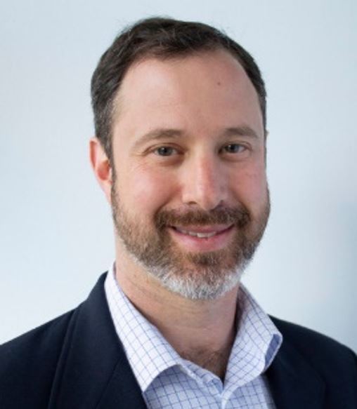 Portrait of Director Adam Bovilsky in suit coat smiling at camera