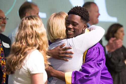 Young man hugging woman on stage at graduation
