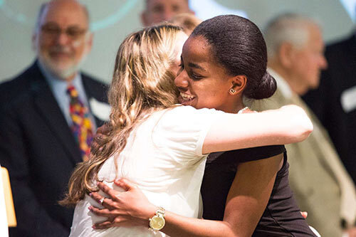 Young woman graduating on stage hugging woman