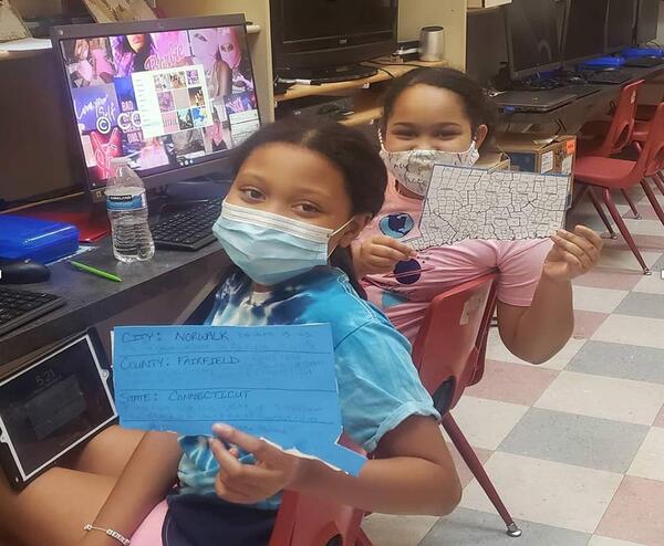 2 girls at computers showing their work wearing covid masks