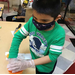 Boy pressing down on art project on table wearing gloves and covid mask