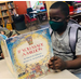 boy reading book at table wearing backpack and covid mask