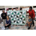 Seniors and children standing around and holding a completed quilt in a room
