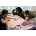 2 children and 2 senior women working on a quilt together on a table inside