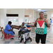 Senior women inside working on quilts at tables and one senior woman standing showing her quilt patchwork and looking at camera