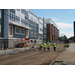 4 construction workers walking along a dirt road, past the freshly sided building 